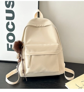 Detail of cream leather backpack with fuzzy charm and front pocket in minimalist setting