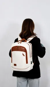 Detail of cream canvas backpack featuring brown leather accents and a built-in USB charging port