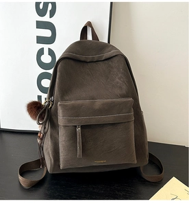 Close-up of dark brown vintage backpack featuring white contrast stitching and a plush ball charm