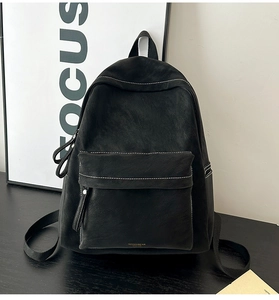 Detail of black faux suede backpack featuring white contrast stitching and a front zip pocket