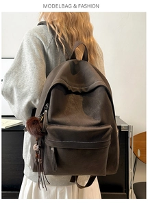 Detailed view of dark brown PU backpack featuring side pompom and decorative white stitching
