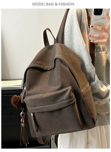 Side view of dark brown pebbled faux leather backpack with pompom and tassel detail