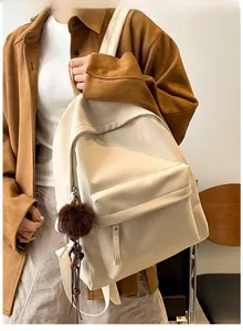 Detail shot of a cream-white PU leather backpack featuring a plush brown pompom charm