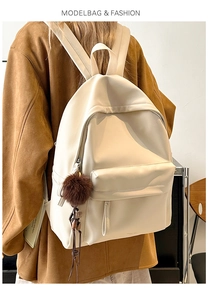 Close-up of cream PU leather backpack featuring a plush ball and fringe zipper charm