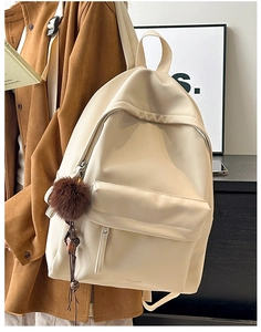 Side view of cream PU leather backpack with a plush pom-pom charm being worn over a coat
