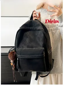 Detail of a vintage black PU leather backpack with contrast stitching and pompom charm