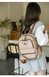Beige travel backpack with brown leather trim shown on a model in a cafe setting