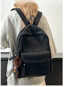 Close-up of black PU backpack with white stitching details and plush ball charm