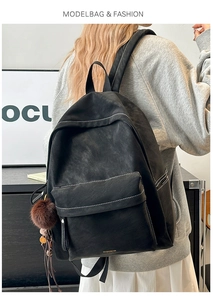 Side view of a large black matte PU leather backpack with white stitching on a model