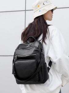Detail of black lychee grain PU leather backpack with silver zippers and tassel accent