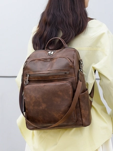 Detail of dark brown faux leather backpack showing pebbled texture and functional zippers