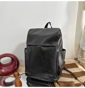 Close-up of black PU leather backpack showing flip-top lid and dual snap button closures