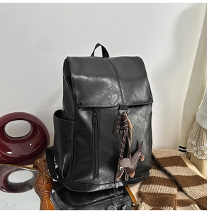 Close-up of black PU leather backpack with flip-top cover and cute puppy charm hanging