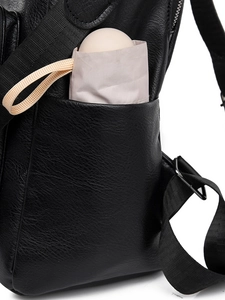 Detail of black pebbled PU leather backpack with side pocket holding a pink mini umbrella