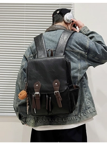 Detail eines schwarzen Vintage-Lederrucksacks mit braunen Schnallen und Bärenanhänger