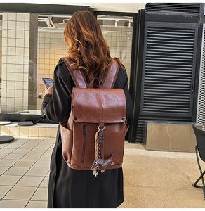 Brown faux leather travel backpack with dog charm accessory shown on a model's back