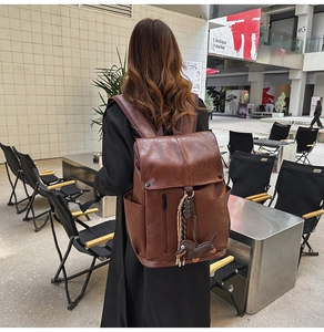 Close-up of brown PU leather backpack with a decorative dachshund puppy charm in outdoor setting
