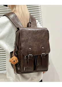 Detail of vintage brown leather backpack with front zip pockets and plush puppy charm