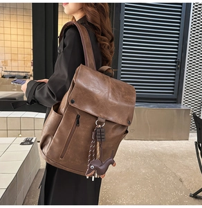 Detail of dark brown faux leather backpack with flap closure and dog charm on urban model