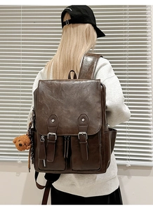 Detail eines Retro-Rucksacks aus braunem PU-Leder mit Magnetschnallen und Bärenanhänger