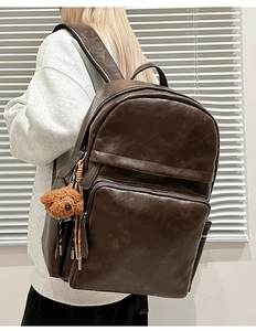 Detail of vintage brown leather backpack with multiple zippers and a cute bear charm
