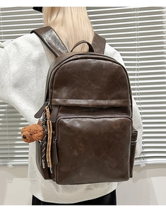 Detailed view of dark brown leather backpack with a cute bear plush keychain accessory
