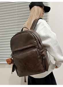 Detail of dark brown leather backpack with front zipper pocket and plush bear pendant