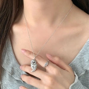 Gros plan détaillé d'un collier pendentif chouette argenté et d'une bague avec gemme