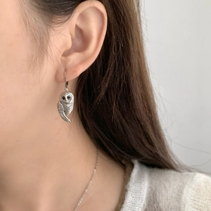 Détail d'une boucle d'oreille hibou en argent portée avec texture plume et crochets