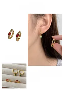 Détail macro de boucles d'oreilles dorées avec pierres vertes carrées et rouges ovales