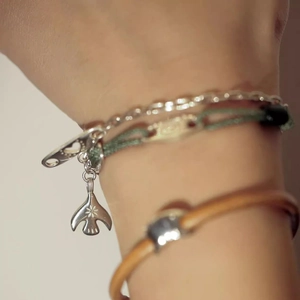 Gros plan d'un bracelet multicouche avec pendentif oiseau en argent et corde verte