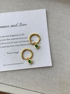 Gros plan de boucles d'oreilles créoles dorées avec pendentifs en pierre verte carrée