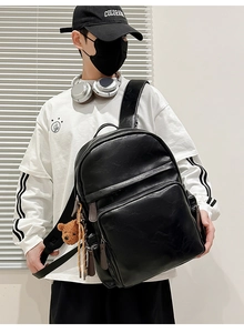 Close-up of black PU leather backpack with a brown plush bear charm and matte texture