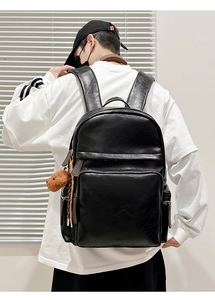 Rear view of a model wearing a large black glossy faux leather backpack with bear charm