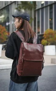 Detail view of burgundy leather commuter backpack with zipper on urban street background