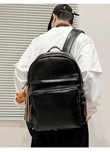 Detail of black faux leather backpack with lychee texture and cute brown bear pendant