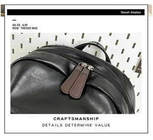 Detail view of the black PU leather backpack with long brown zipper pulls and top handle