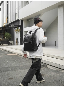 Minimalist black leather backpack for men shown in a modern urban street setting