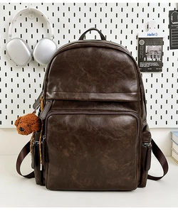 Detail of a dark brown vintage faux leather backpack with a plush bear charm on a desk