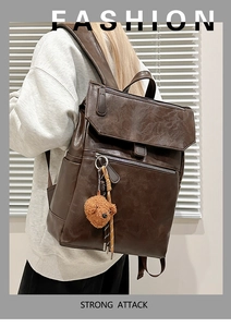 Detail of dark brown vintage backpack featuring leather texture and a plush bear charm