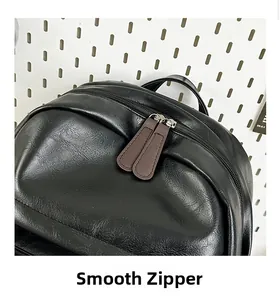 Close-up of black PU leather backpack showing smooth dual zippers with brown pull tabs