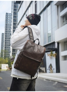 Deep brown faux leather backpack worn by a male model in a modern urban street setting