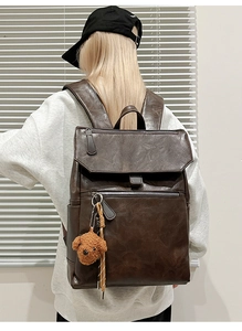 Close-up of dark brown leather backpack featuring a vintage texture and a cute bear charm