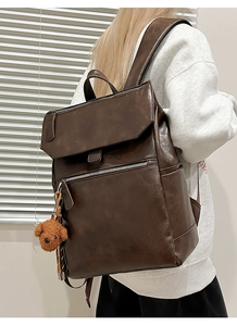 Close-up of a large dark brown PU leather backpack with a cute plush dog charm