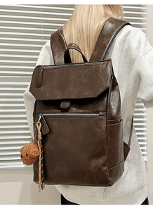 Detail of vintage dark brown leather backpack with teddy bear charm and textured finish