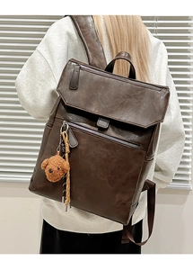 Detail of dark brown leather backpack with teddy bear charm and soft window lighting
