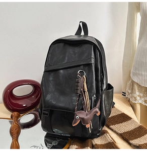 Detail of black faux leather backpack featuring a diagonal zipper and dog bag charm