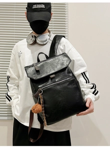 Detail of black PU leather backpack featuring front zipper pocket and brown fluffy keychain