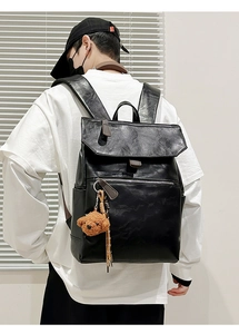 Detail of black leather backpack featuring flap cover and brown plush bear charm