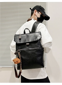 Detail of black faux leather backpack featuring a flip-top cover and a plush bear charm